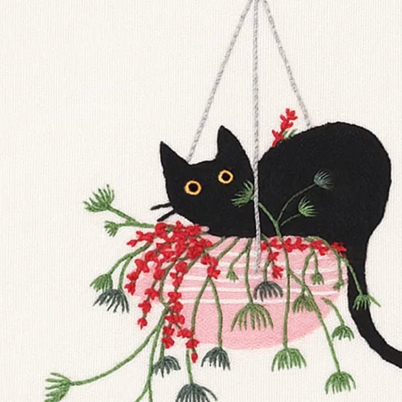 Embroidery of a black cat with red flowers on a white background