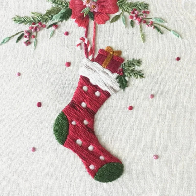 Embroidered Christmas stocking with a gift and floral decorations on a white background