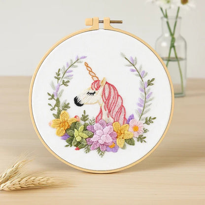This embroidery design features a graceful unicorn with a soft pink mane and a golden horn, surrounded by a vibrant floral wreath. The mix of yellow, purple, and green blooms creates a harmonious and dreamy atmosphere — perfect for adding a touch of magic and elegance to any space.