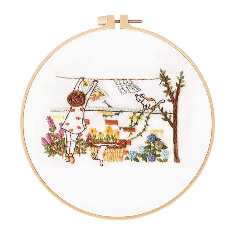 Embroidery hoop with a colorful garden scene including a cat, flowers, and a tree.