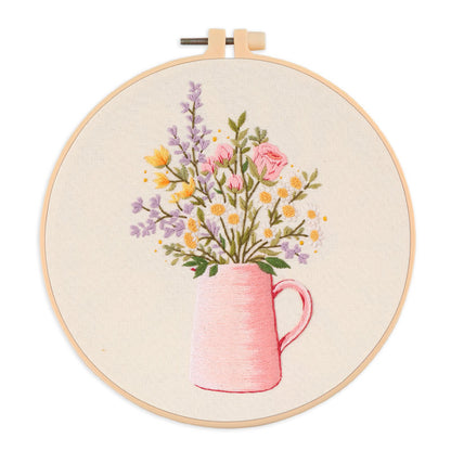 Embroidery hoop with a floral design of a pink mug and flowers on beige fabric.
