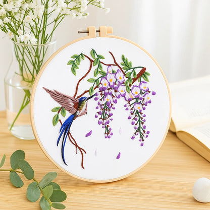 Embroidery hoop with a hummingbird and wisteria design on a wooden surface.