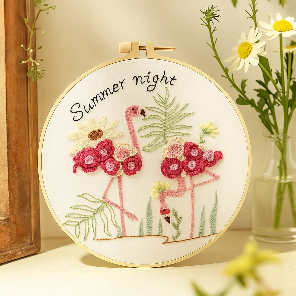 Embroidery hoop with flamingo design and 'Summer night' text, surrounded by flowers.