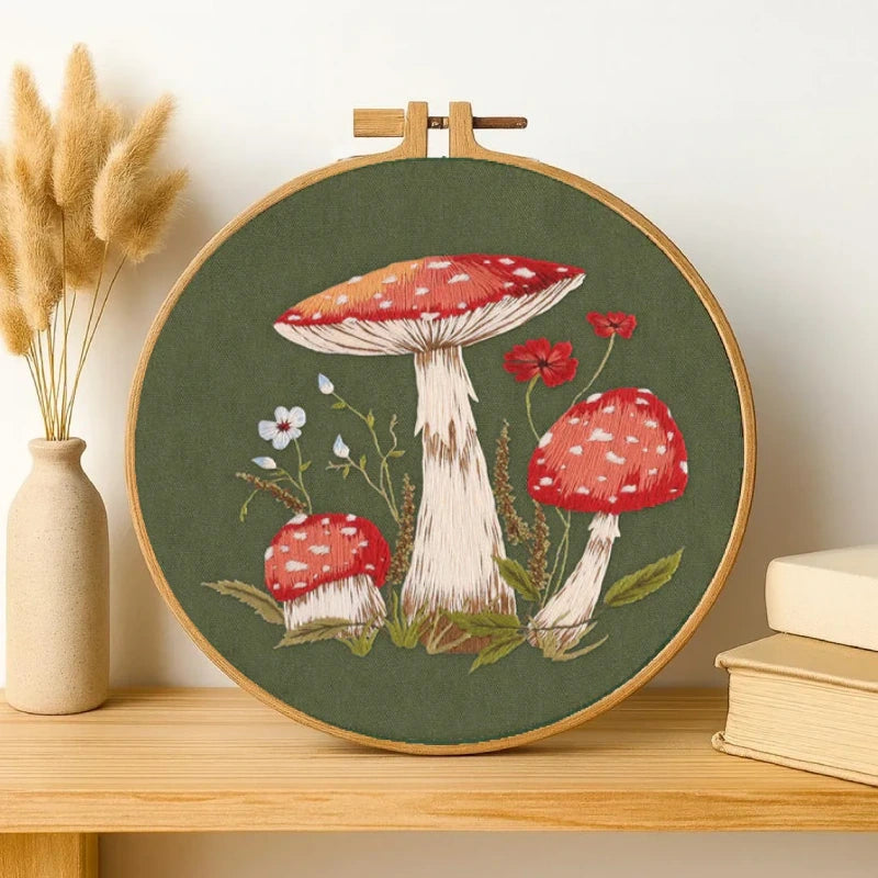 Embroidery hoop with mushroom design on a wooden shelf.