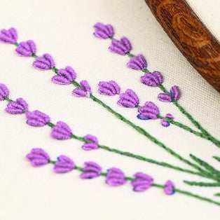 Embroidery of lavender flowers on fabric with a wooden hoop.