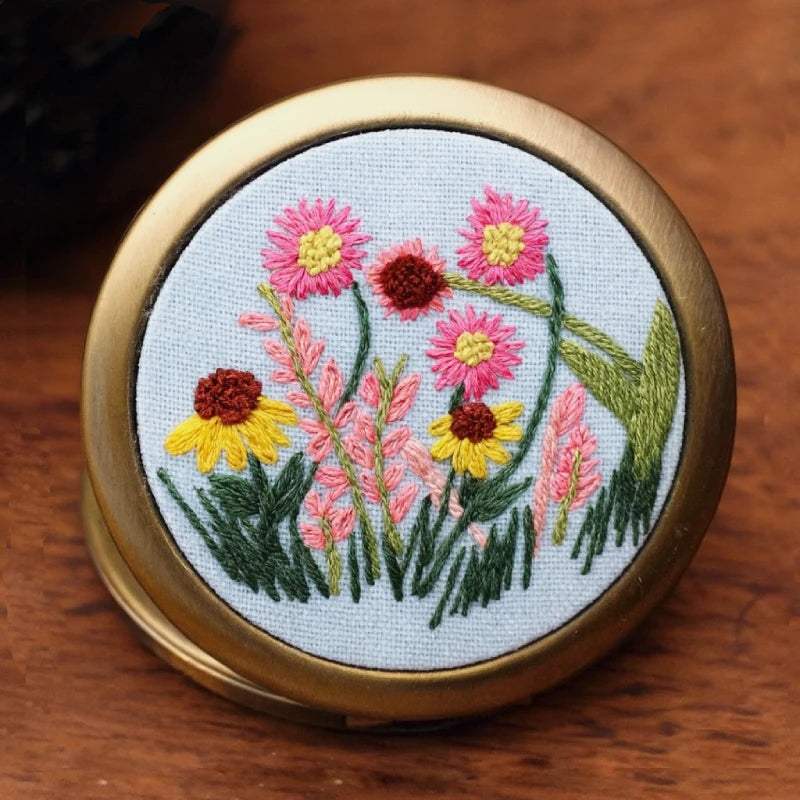 This delicate hand-embroidered compact mirror captures the essence of a summer meadow in full bloom. The lively pink, yellow, and coral flowers sway gracefully among lush green leaves, bringing a touch of nature’s poetry into your daily routine. Small yet exquisite, it’s perfect for carrying beauty — and serenity — wherever you go.