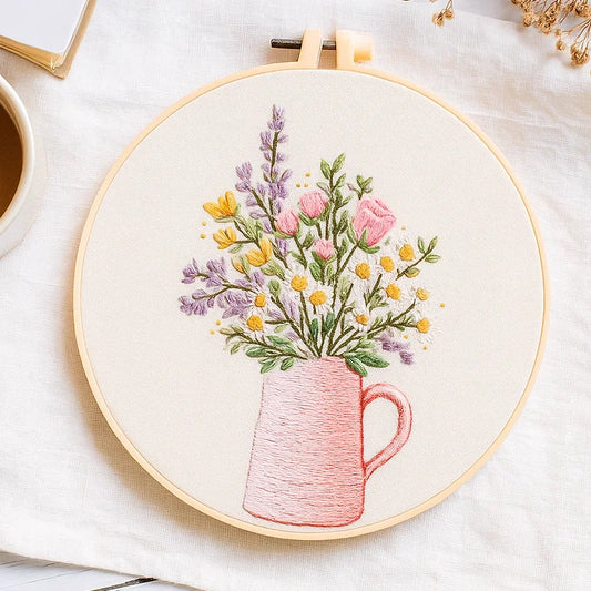 Embroidery hoop with floral design of a pink mug and flowers on a white background