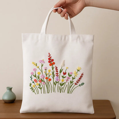 White tote bag with floral embroidery held by a hand on a wooden surface.