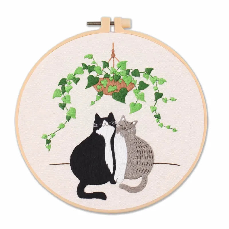 Embroidery hoop with two cats and a plant design on a white background